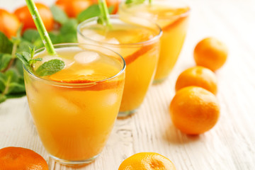 Three tangerine cocktails with ice, mint and straws on a white wooden table, close up