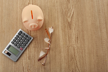 Beige piggy bank with glasses and calculator on wooden background