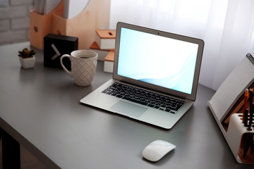 Fototapeta premium Workplace with laptop, table, mouse and cup beside the window