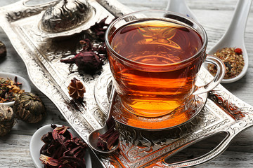 Tea concept. Glass cup of tea with different kinds of dry tea on vintage tray, close up
