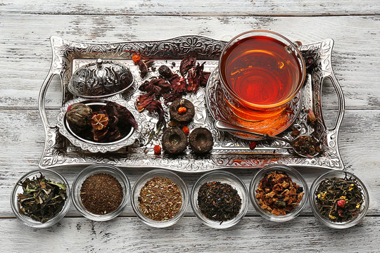 Tea concept. Glass cup of tea with different kinds of dry tea on vintage tray, close up