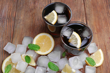 Two glasses of cola with cubes of ice and lemon on wooden table background