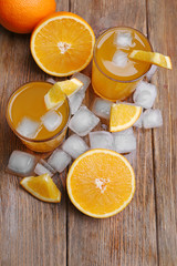 Two orange juices with cubes of ice and orange on wooden table background