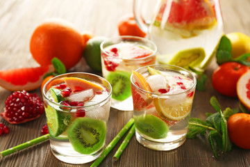 Refreshing cocktails with ice, pomegranate seeds and slices of fruits on wooden background
