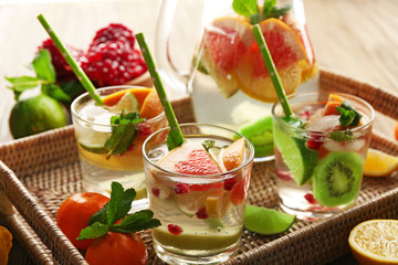 Refreshing cocktails with ice, mint, pomegranate seeds and slices of fruits on wicker tray