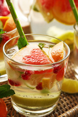 Refreshing cocktail with ice, mint, pomegranate seeds and slices of fruits on wicker tray