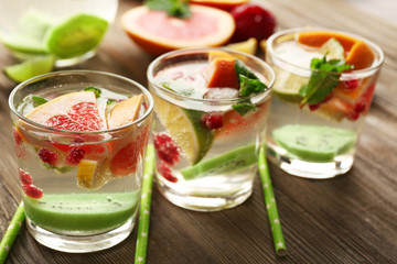Refreshing cocktails with ice, mint, pomegranate seeds and slices of fruits on wooden background