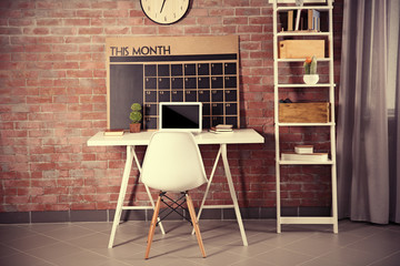 Workplace with laptop, table and calendar board on brick wall background