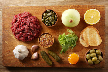 Beef tartare ingredients on wooden cutting board