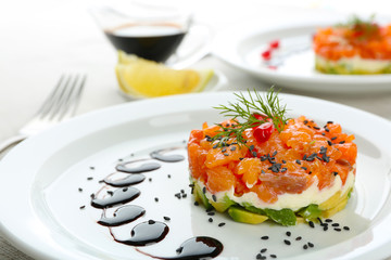 Fresh tartar with salmon, avocado and soy sauce on white plate, close up