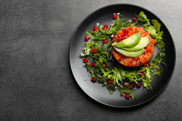 Fresh tartar with salmon, avocado and arugula on black plate