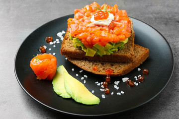 Fresh tartar with salmon, avocado and black bread on plate
