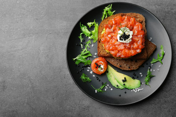 Fresh tartar with salmon, avocado, black caviar and black bread on plate
