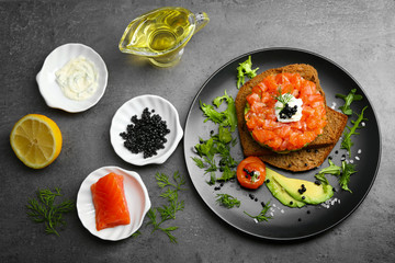 Fresh tartar with salmon, avocado, black caviar and black bread on plate
