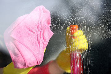 Woman in rubber glove cleaning window with sponge and detergent, close up