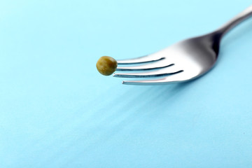 Silver fork with single pea on blue background