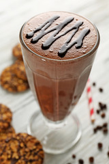 Glass of chocolate milkshake with cookies and coffee beans on wooden table closeup
