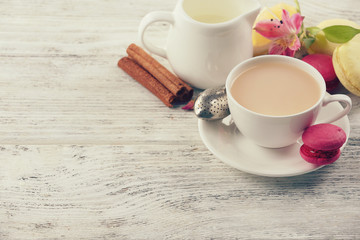 Cup of brewed tea with milk and macaroons on light wooden table