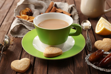 Cup of brewed tea with milk, spices and cookies on wooden table