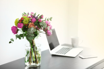 Jar of roses on table beside laptop