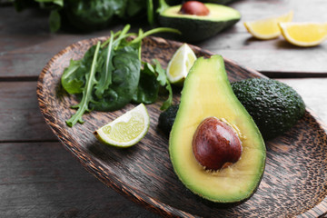 Sliced avocado with lime, spinach and arugula on wooden plate