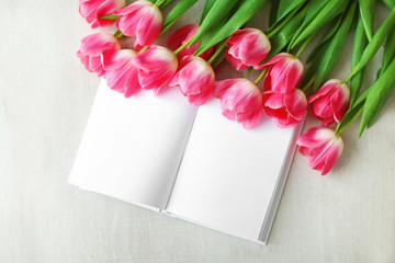 Pink fresh tulips and notebook on the white table, top view