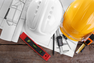 Two helmets and blueprint on a wooden background.