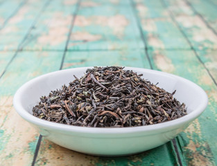 Loose dried darjeeling black tea leaves in white bowl over wooden background