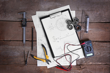 Digital multimeter and blueprints on a wooden background.