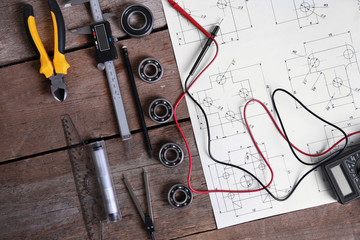 Digital multimeter and blueprint on a wooden background.