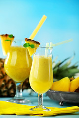 Pineapple smoothie in cocktail glasses with slices on blue blurred background