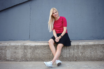 Fototapeta premium Young happy beautiful blonde woman sitting on the concrete river pier and looking into camera