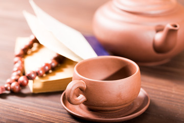 Ceramic tea-things, beads and the book on a wooden table