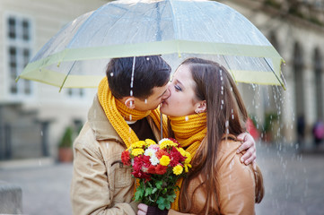 Closeup of young beautiful couple kissing under umbrella