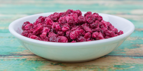 Dried pomegranate seeds in white bowl over wooden background