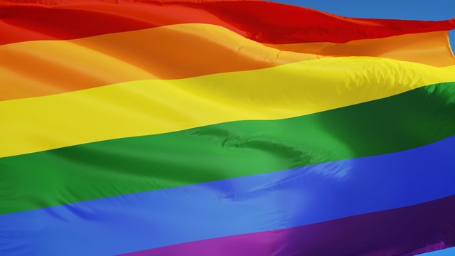 The gay pride rainbow flag waving in slow motion against clean blue sky, seamlessly looped, close up, isolated on alpha channel with black and white luminance matte, perfect for film, news