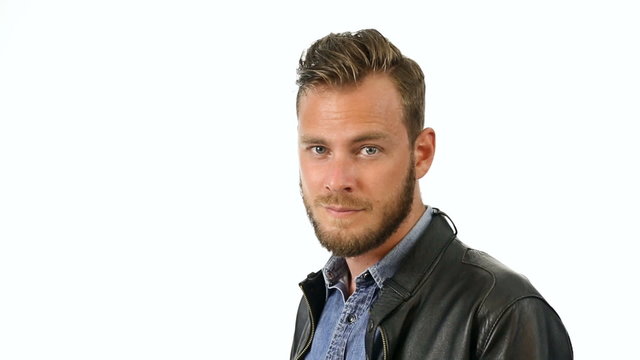 A trendy man wearing a jeans shirt and a black leather jacket, standing in front of a white background looking at camera, feeling calm and laid back.