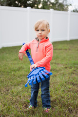 Little girl holding a blue toy rake helping with yard work. 