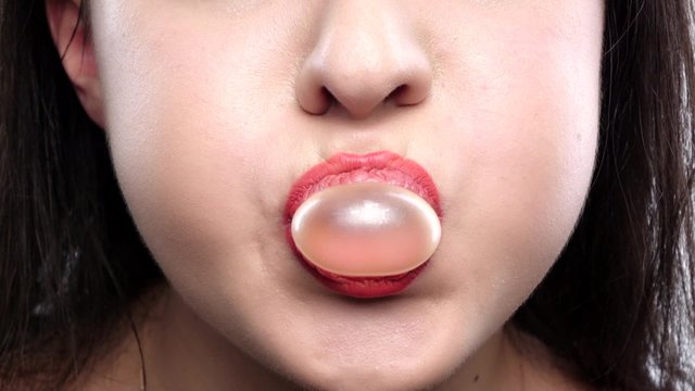 Young girl with yellow chewing gum on white background. Close up. Slow motion