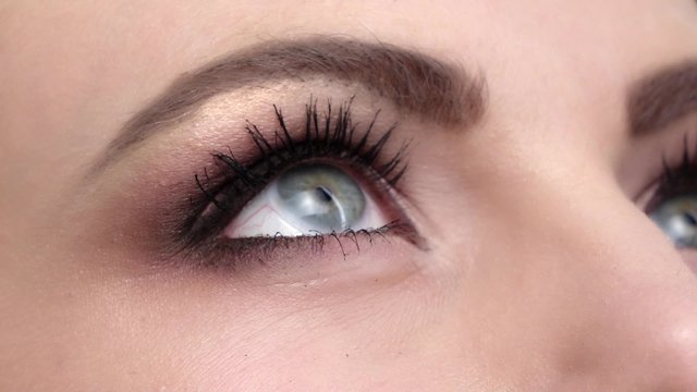 Woman with beautiful blue eyes and long black eyelashes and bright make, contact lenses, close up, slow motion