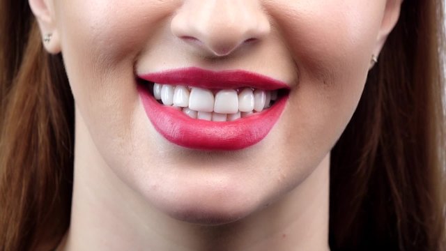 Beautiful smiling young woman with perfect skin, red lipstick and teeth. Close up. Slow motion