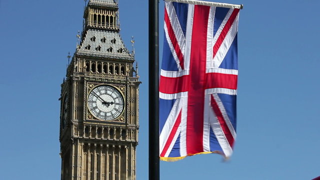 Big Ben clock face, on the Elizabeth Tower, with a Union Jack flag flying above the Houses of Parliament in London England