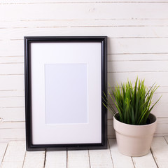 Black empty frame and grass in pot on white wooden background.
