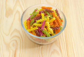 Uncooked colored spiral pasta in a glass bowl