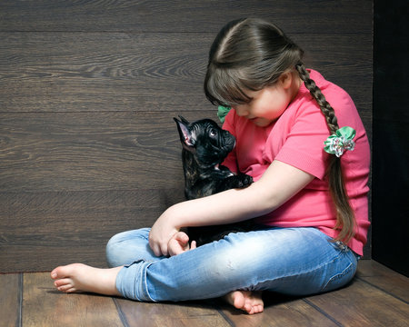 Girl with a black dog on the floor near the wooden walls. The dog - french bulldog puppy. Girl in jeans, barefoot. Dog and little mistress. Girl full 
