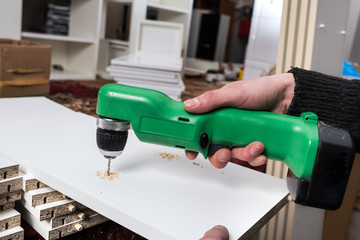 Carpenter drills a hole in the component parts of a white kitche