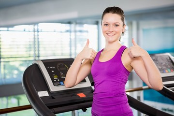 Smiling brunette with thumbs up standing on treadmill