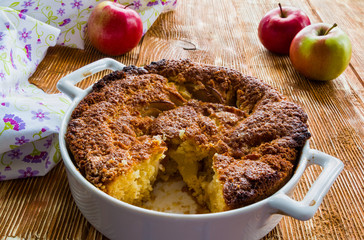 Apple pie in a white baking dish on the wooden background.