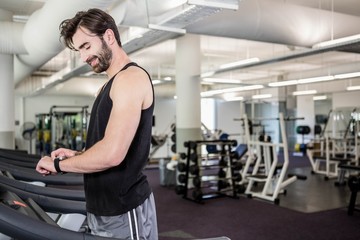 Fototapeta na wymiar Smiling man on treadmill looking at smartwatch