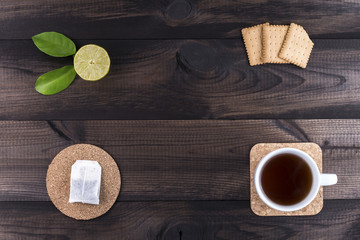 cup of tea with tea cookies, fresh lime and bag of tea on wooden background